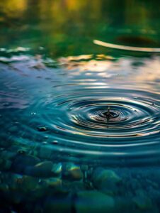 Minimalist image of a single droplet falling into still blue water, with soft ripples and gentle light symbolizing calm, connection, and the ripple effect of healing.