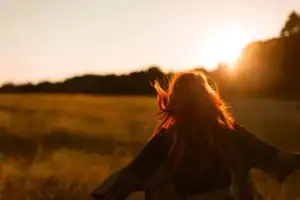 woman in field at sunrise with arms open