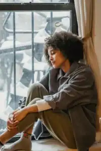 woman sitting on windowsill looking out at snow on ground
