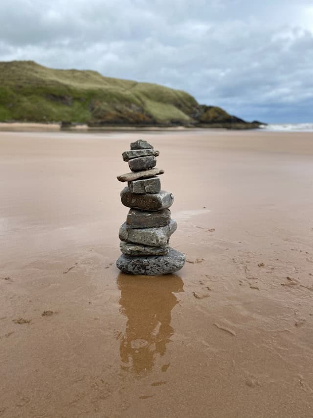 Carefully balanced stones stacked on wet sand, representing achievement that never feels stable enough